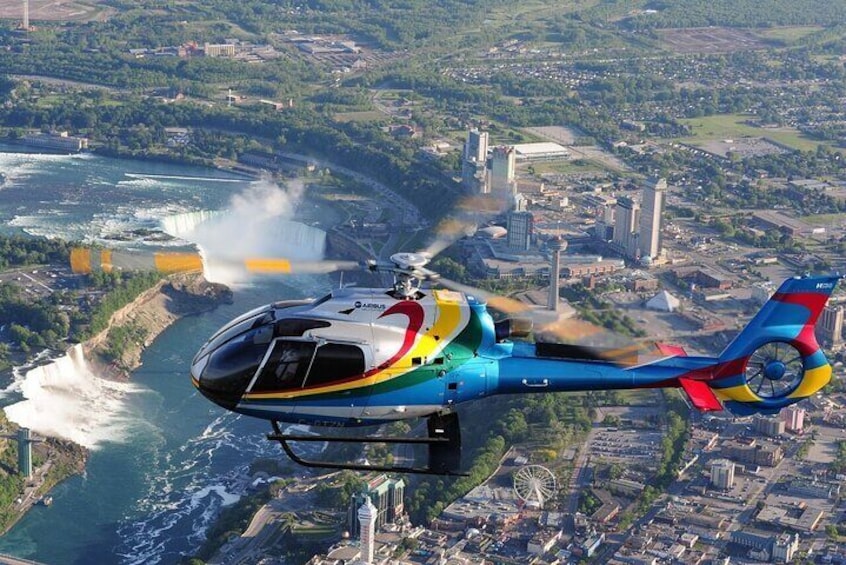 Un helicóptero colorido vuela sobre una ciudad costera con una cascada al fondo. 4