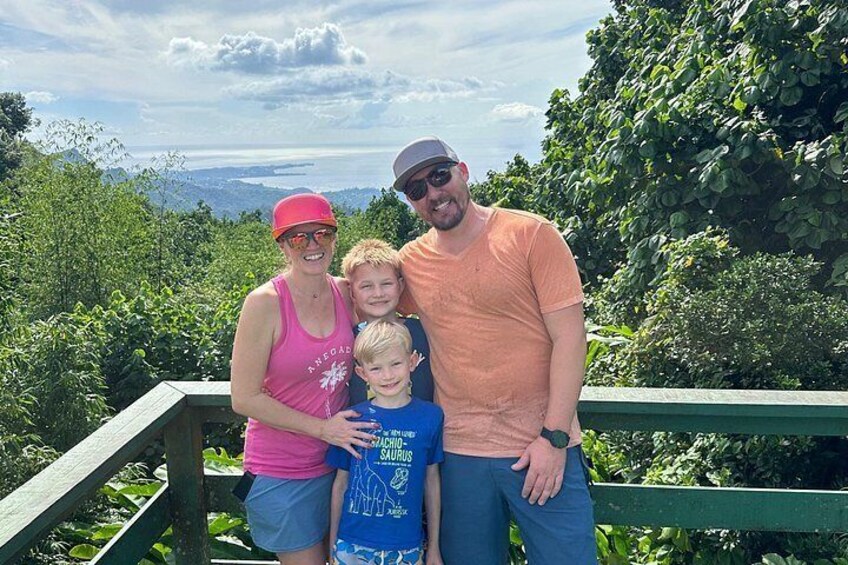 A family of four on a wooden deck with a scenic view of a forest and a body of water in the background. 5