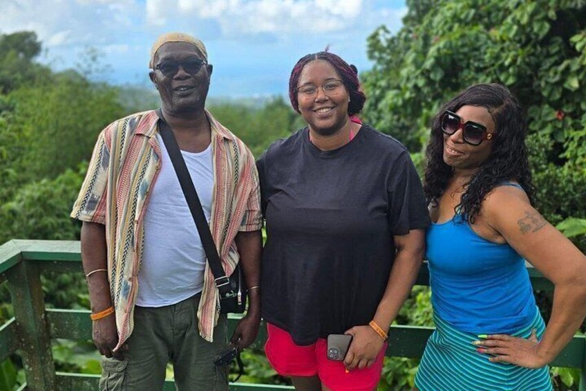 Three people standing on a wooden deck with greenery in the background. 3