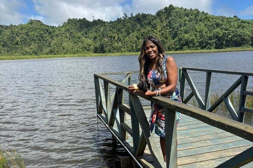 A woman standing on a wooden dock over a body of water, with a forested hill in the background. 3