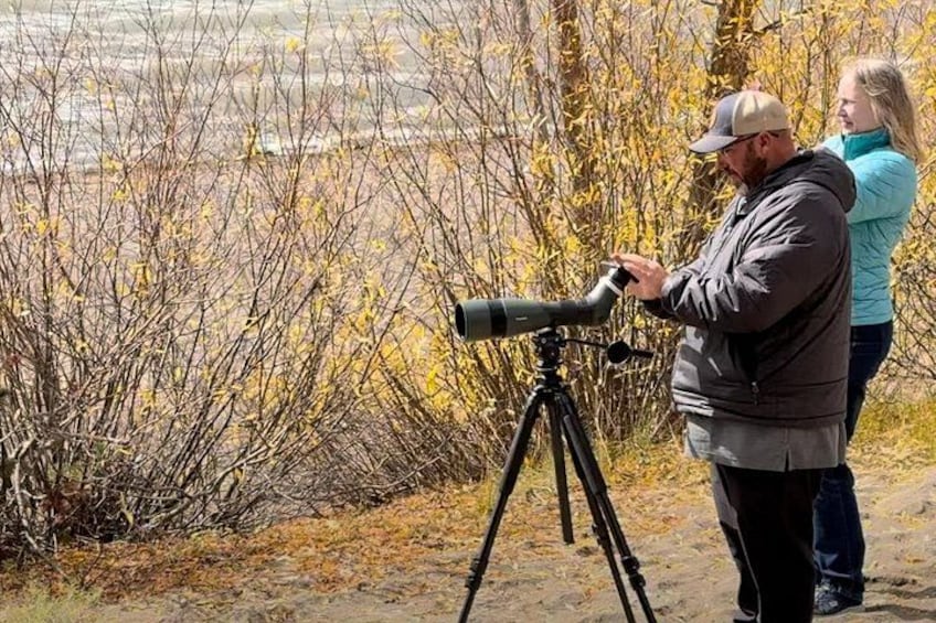 En person använder ett teleskop som är monterat på ett stativ i en naturlig miljö med sparsam växtlighet. 2