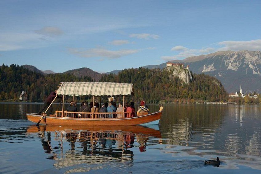 A wooden boat with passengers on a calm lake, surrounded by mountains and a church. 3