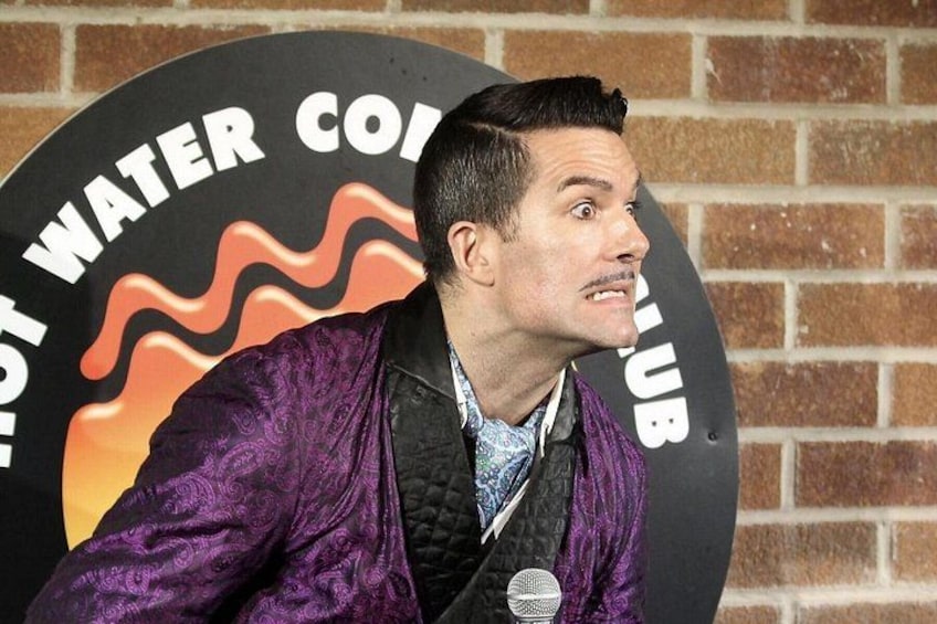 Une personne portant une veste violette parle dans un microphone, avec en arrière-plan une image qui comprend le texte « HOT WATER CLUB ». 3