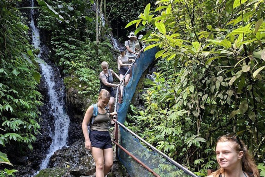 Un grupo de personas caminando por un puente de madera sobre un salto de agua en una zona boscosa. 2