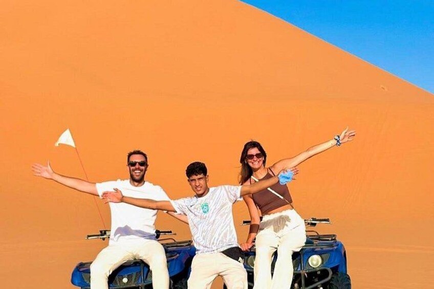Tre personer i en sandbuggy, med en flagga, i ett ökenlandskap under en klar himmel. 3