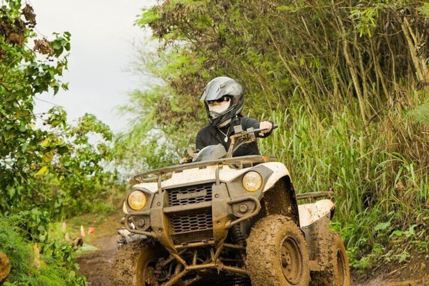 A person riding a four-wheeled off-road vehicle through a muddy path surrounded by greenery. 2