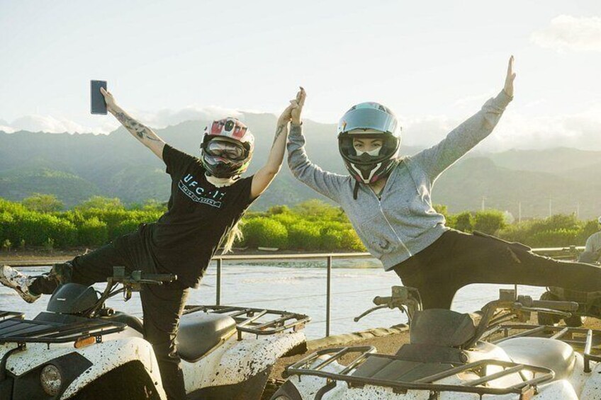 Two people on ATVs with a river and mountains in the background. 4