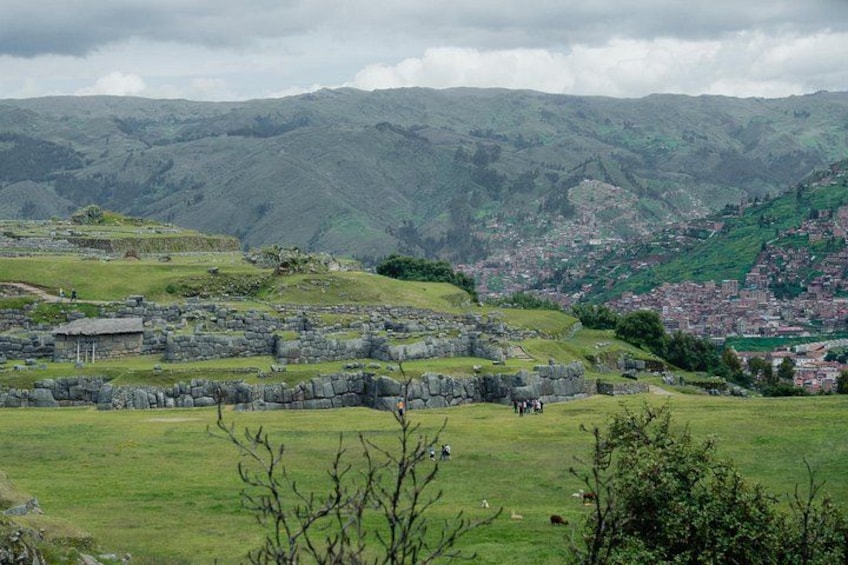 A rural landscape with stone ruins, a green field, and a distant town. 1