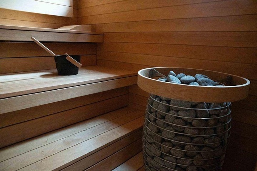 A sauna with wooden benches, a metal ashtray, and a stone-filled container. 2