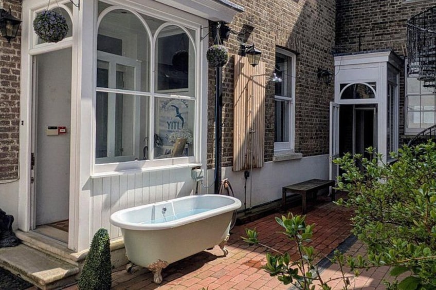 A Victorian-style house with a white bathtub outside, a brick pathway, and a small garden. 3