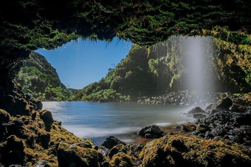 A cave opening to a serene lake with a waterfall, surrounded by lush greenery. 1