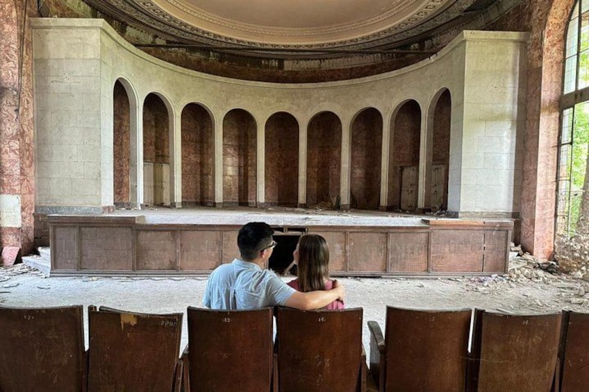 An abandoned theater with a stage and rows of empty seats. 3