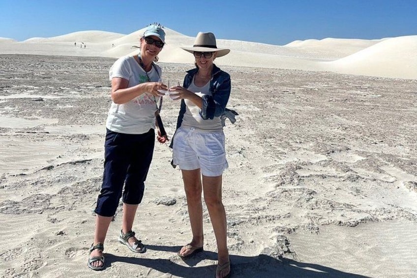 Two people standing on a sandy desert landscape with dunes in the background. 5