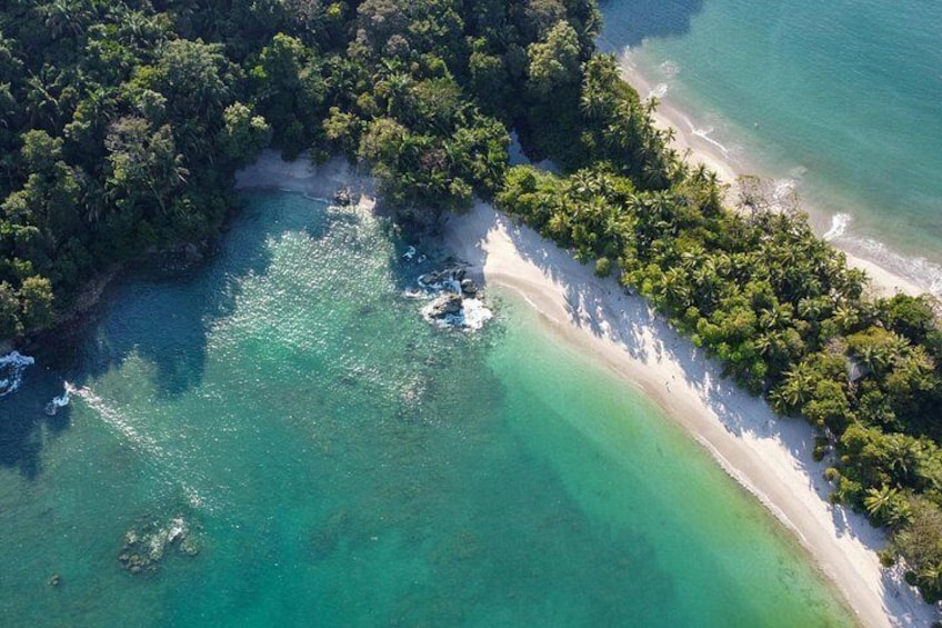Eine Vogelperspektive zeigt einen Strand mit klarem türkisblauem Wasser, einem sandigen Ufer und dichter grüner Vegetation. 4