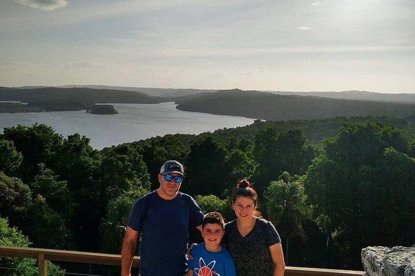 A family of three standing on a wooden deck overlooking a lake surrounded by dense forest. 4