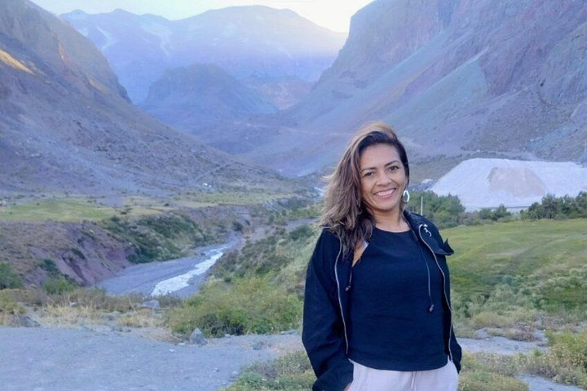 A person standing in a mountainous landscape with a river and snow-capped peaks in the background. 3