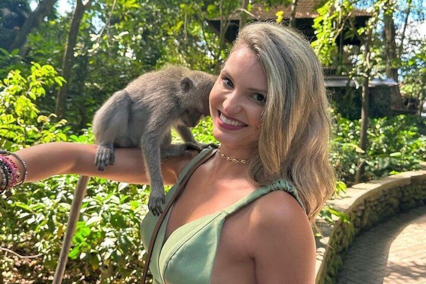 A person with a monkey on their arm, surrounded by greenery and a stone structure. 2