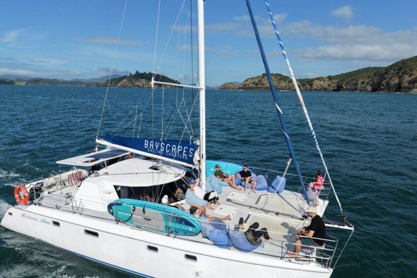 Un velero con el nombre 'BAYSCAPES' en su cubierta, navegando sobre una masa de agua con una costa rocosa al fondo. 4