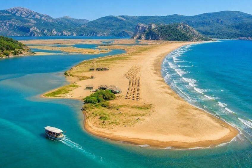 A coastal landscape with a boat on the water, a sandy beach, and mountains in the background. 2
