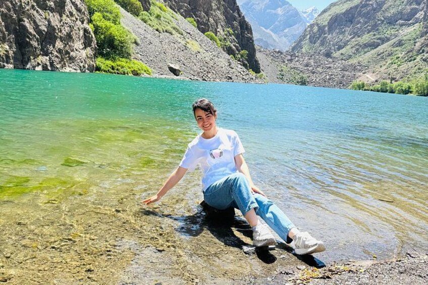 Une personne assise au bord d’un lac aux eaux limpides, avec des montagnes en arrière-plan. 1