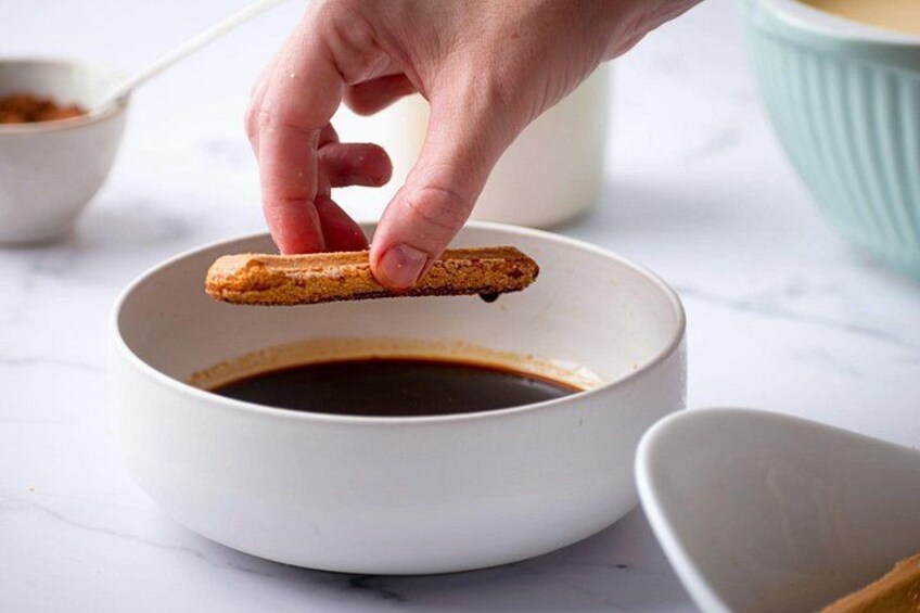 A hand dipping a breadstick into a bowl of dark liquid. 4