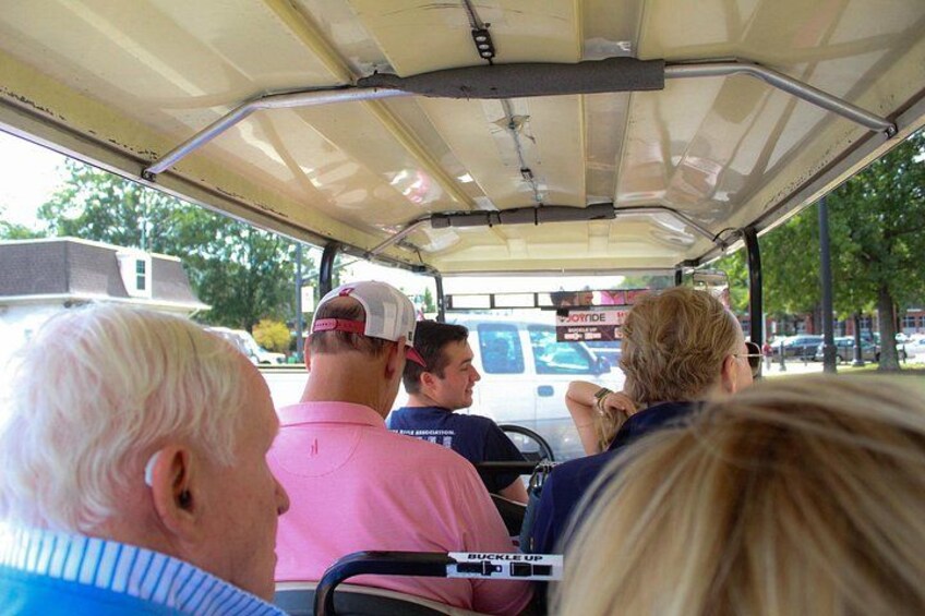 Ein Golfmobil mit Fahrgästen, einem Verdeck und einem Fahrzeug im Hintergrund. 2