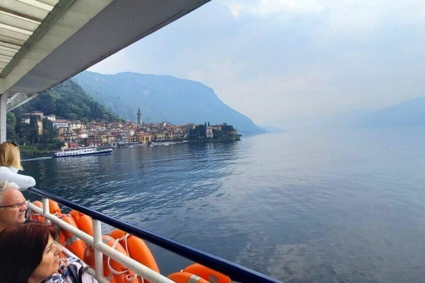 Een boot met passagiers die uitkijken over een kalm meer, een in de verte gelegen stad en bergen. 3