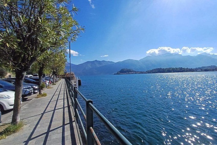 A lakeside walkway with cars parked along the side, trees lining the path, and mountains in the background. 4