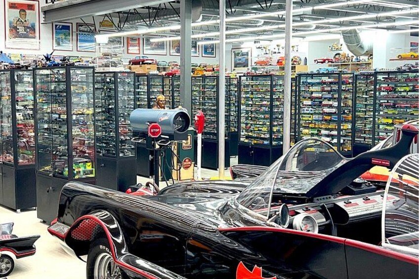 Een oldtimer in een showroom, met glazen vitrines vol speelgoed en verzamelobjecten op de achtergrond. 2