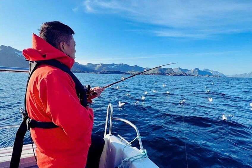 A person in a red jacket fishing on a boat with a mountainous landscape in the background. 4