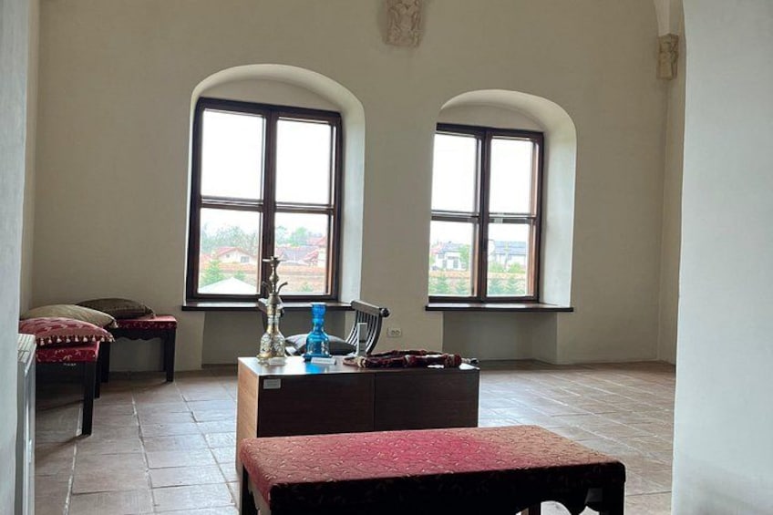 A room with two arched windows, a wooden bench, a table with a red cloth, and a blue bottle. 5