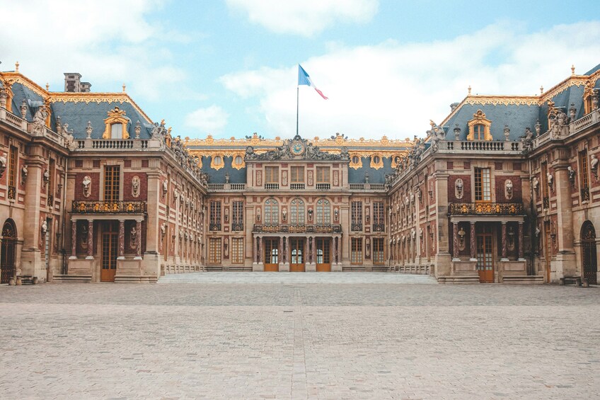 A grand historic building with ornate architecture, a central entrance, and a flagpole with a flag. 1
