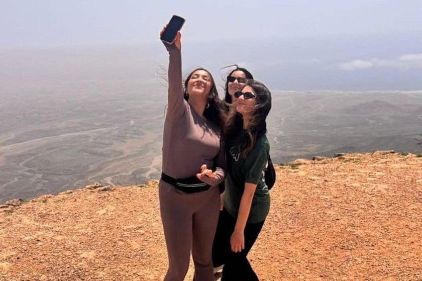 Två personer som tar en selfie på en klippavsats med ett vidsträckt landskap i bakgrunden. 2