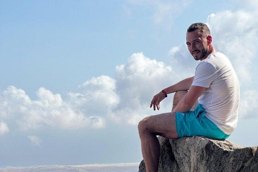 Une personne assise sur un rocher, avec un ciel dégagé et des nuages en arrière-plan. 2