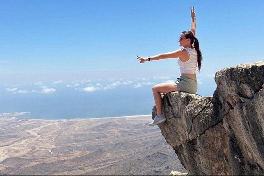 Une personne assise sur un rocher, les bras levés, contemplant un vaste paysage. 1