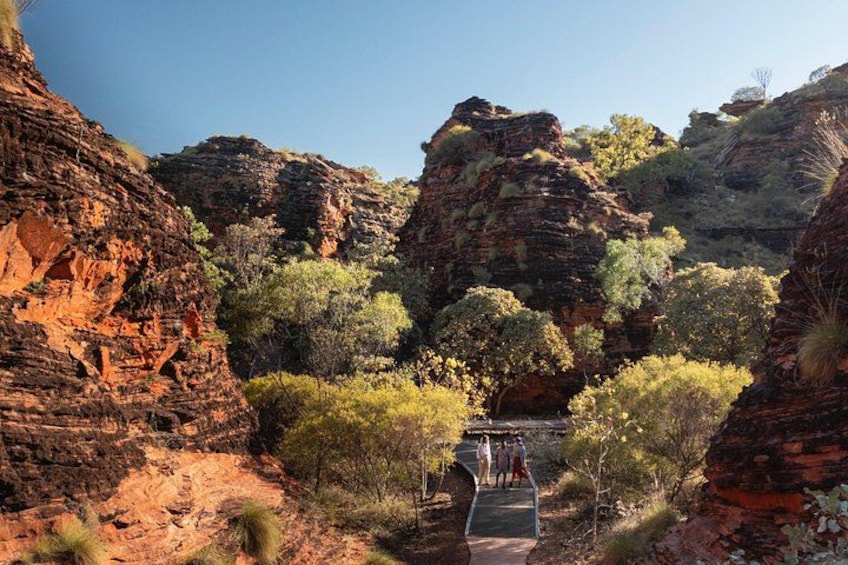 A canyon with red rock formations, green trees, and a paved walkway. 1