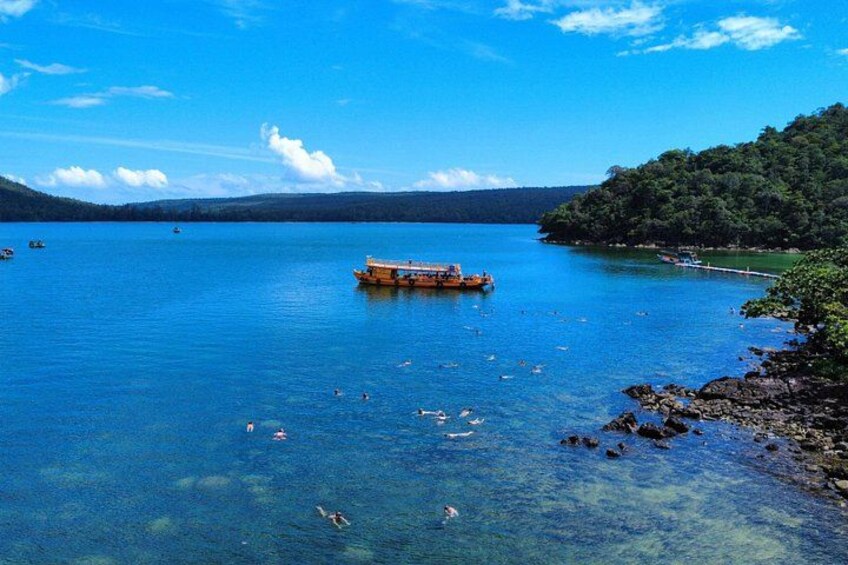A clear blue lake with a boat, rocky shoreline, and distant mountains. 5