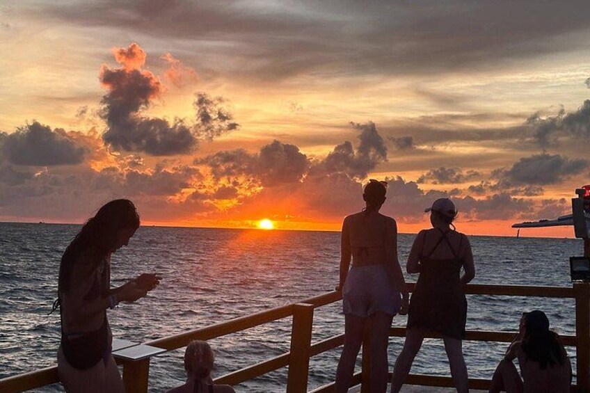 A sunset over the ocean with people standing on a dock. 2