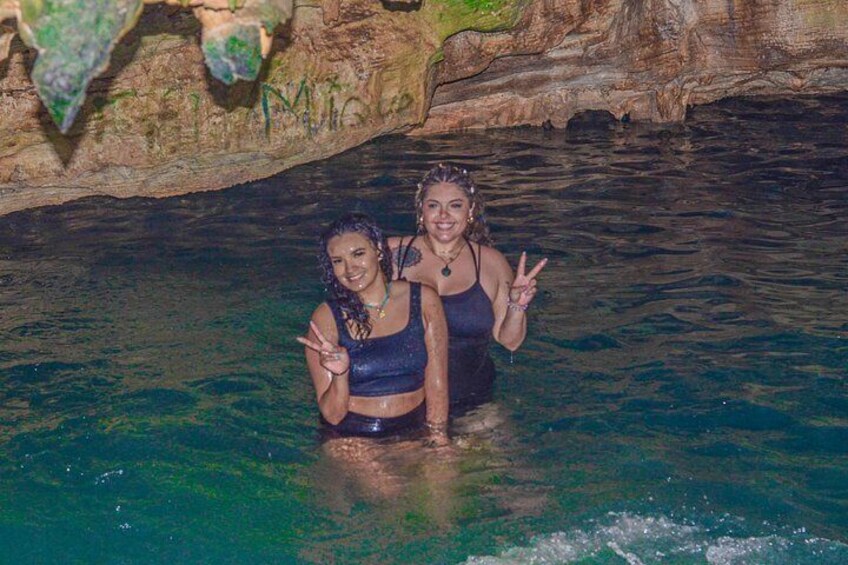 Two people in a clear blue pool with a rocky cave background. 3