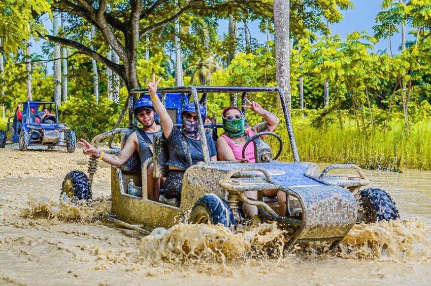 People in an off-road vehicle driving through a muddy area with trees in the background. 2