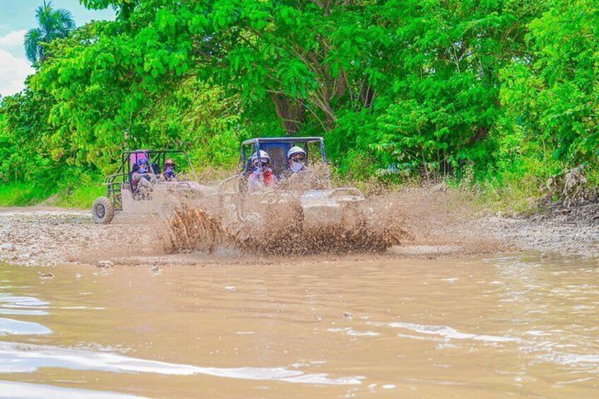 Two off-road vehicles driving through a muddy water crossing. 2