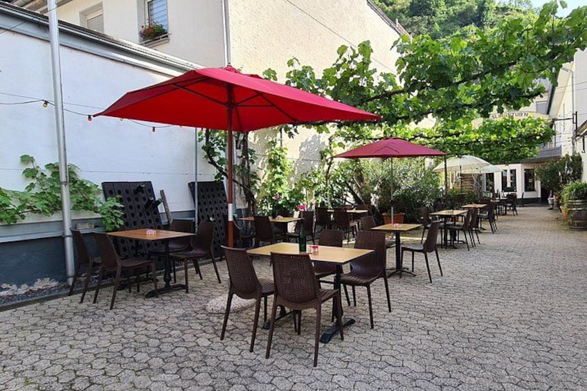 En udendørs café med borde, stole og røde parasoller på en brostensbelagt gulv. 3