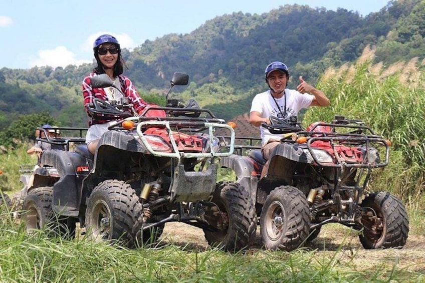 Two people on ATVs in a grassy area with hills in the background. 3