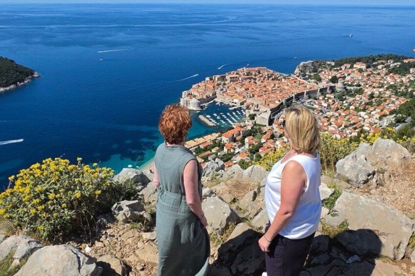 Deux personnes contemplent une ville côtière, avec une forteresse historique en arrière-plan et une vue dégagée sur la mer. 1