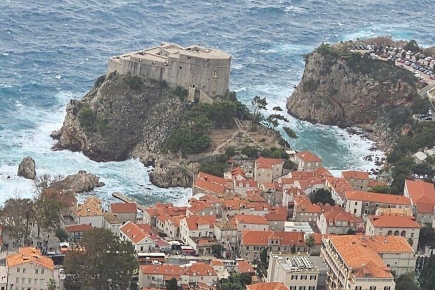 Une ville côtière abritant une imposante forteresse perchée sur un promontoire rocheux, entourée de maisons aux toits de tuiles rouges. 3