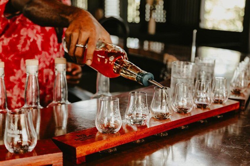 A person pouring a dark liquid into a row of empty glasses on a wooden bar counter. 5