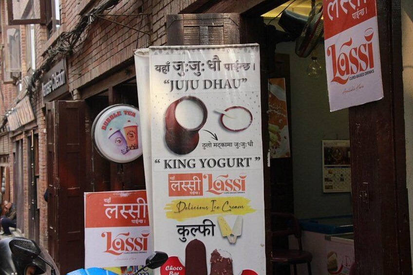 En gade med en butik, der reklamerer for 'King Yogurt' og 'Juju Dhau'. 4