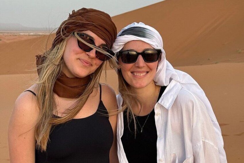Two people standing in a desert with sand dunes in the background. 1