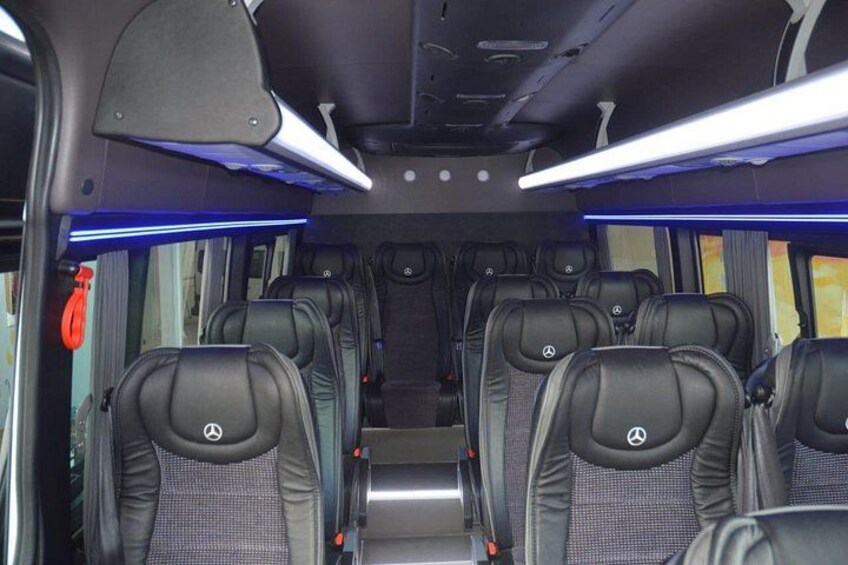 A bus interior with rows of black leather seats, overhead storage compartments, and blue lighting. 4