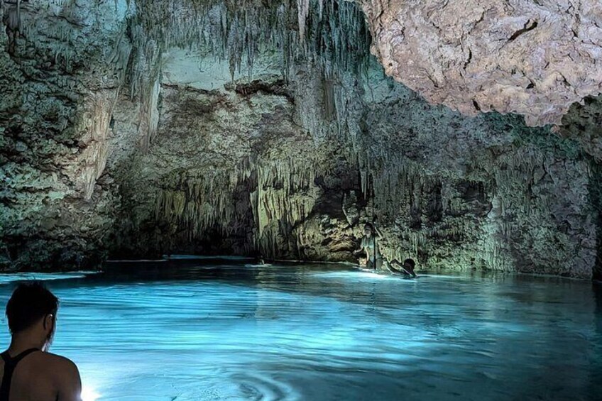 A cave with stalactites and stalagmites, a person swimming, and a large rock formation. 3